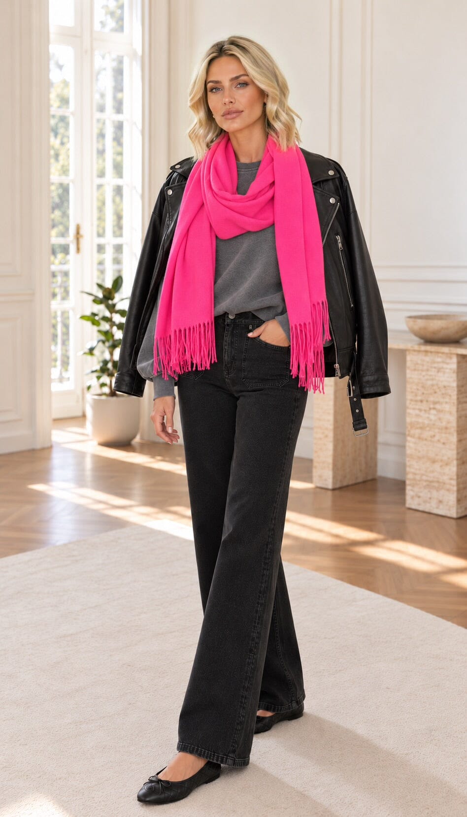 A woman stands in a bright, modern room wearing a loose gray sweatshirt, black wide-leg jeans, and black flats.